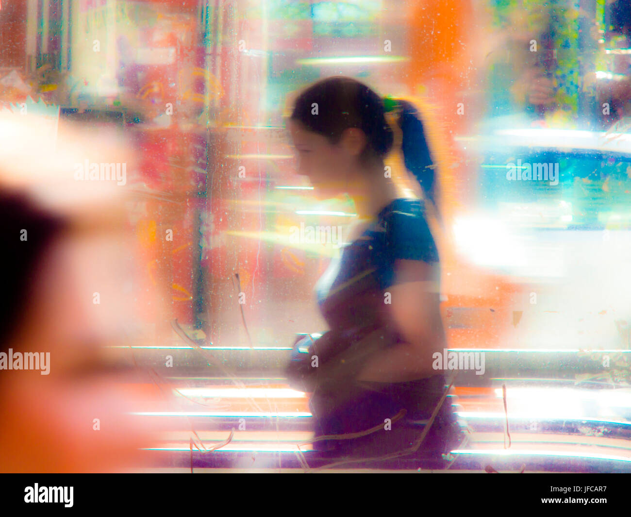 Sfocata giovane donna nelle strade della città in una giornata di sole con colori vibranti, luce ardente e riflessi di vetro Foto Stock