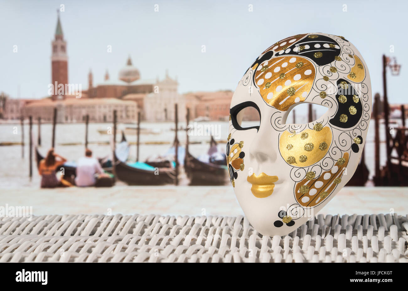 Tradizionale maschera veneziana con gondole attraccate, coppia romantica e la chiesa di San Giorgio Maggiore in sfondo sfocato. Estate calda sensazione di vacanza Foto Stock