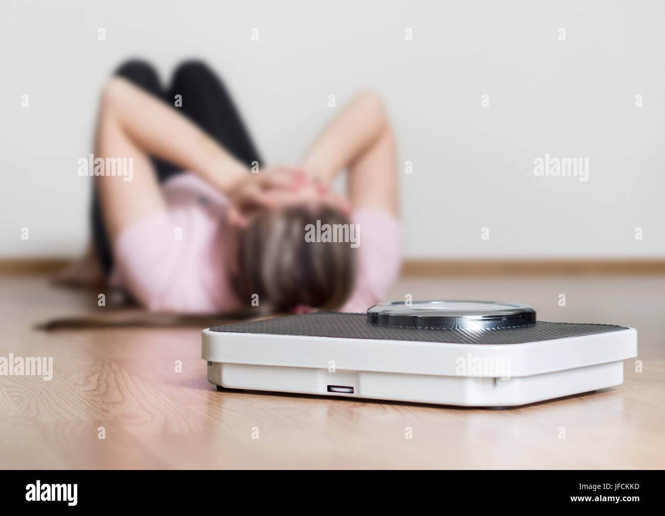 La perdita di peso non concetto. Scala e depresso, frustrato e triste donna seduta sul pavimento tenendo la testa e braccia sulle ginocchia. Foto Stock