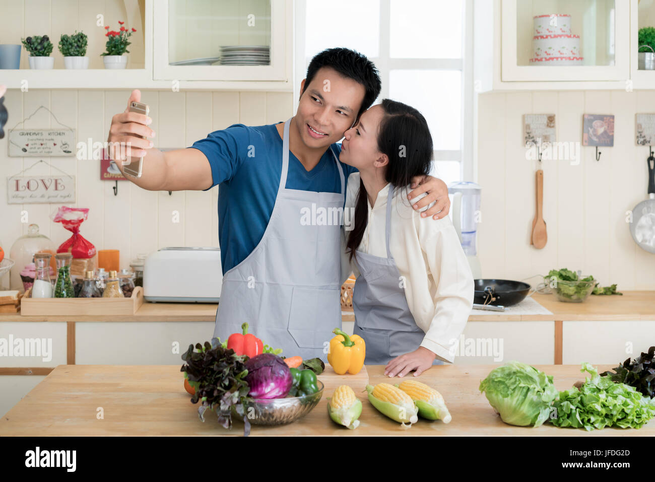 Asian bello ragazzo è sorridente e cottura in cucina mentre facendo selfie utilizza lo smartphone a casa. Felice amore giovane concetto. Foto Stock