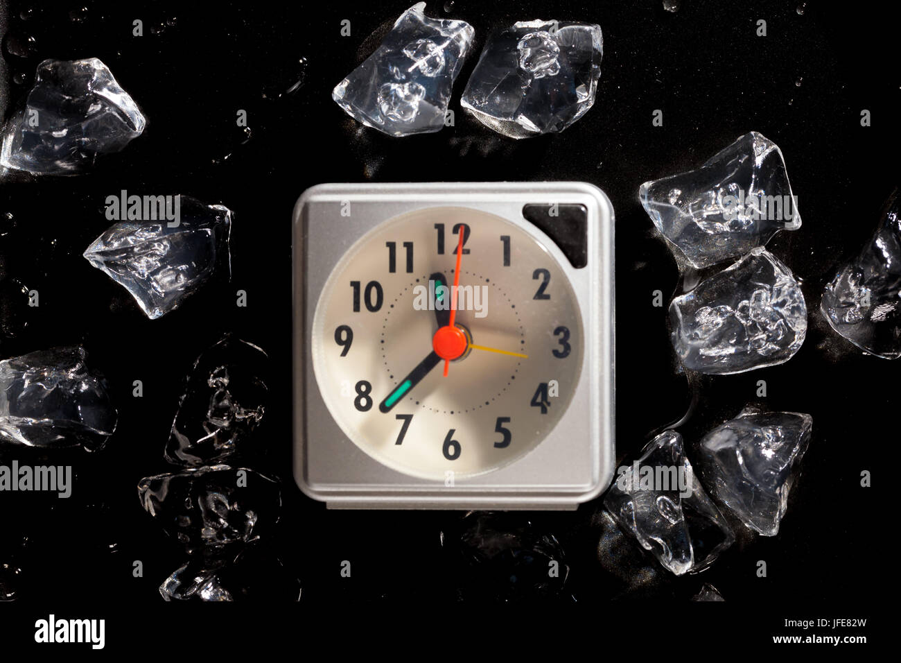 Congelati nel tempo concetto con cubetti di ghiaccio e di un orologio e di acqua di fusione scende su di uno sfondo scuro Foto Stock