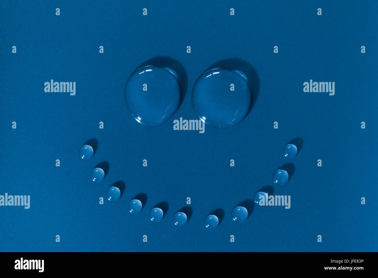La faccina sorridente fatta di gocce d'acqua su uno sfondo blu Foto Stock