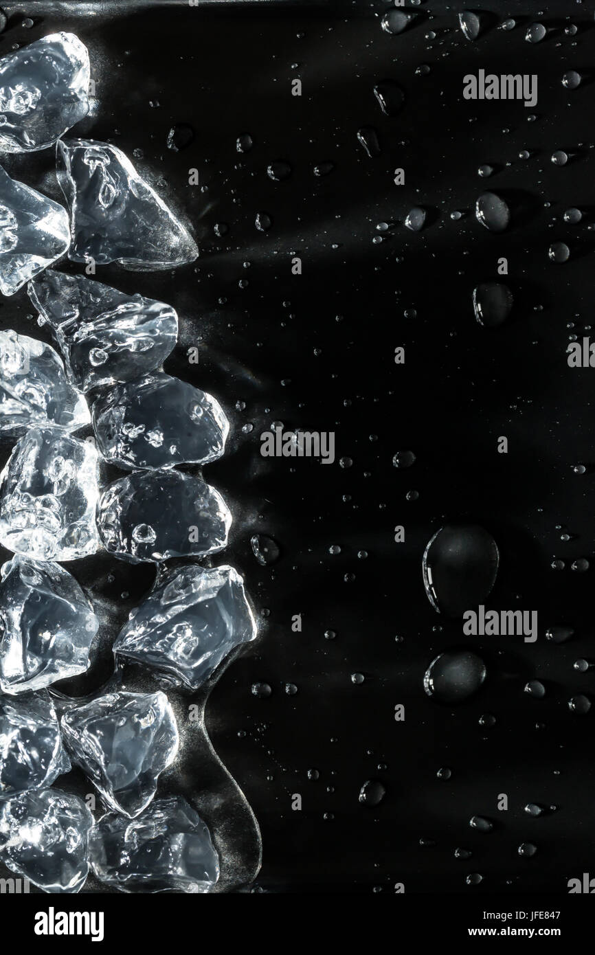 Cubetti di ghiaccio la fusione sul bordo dell'immagine con le goccioline di acqua su sfondo scuro Foto Stock