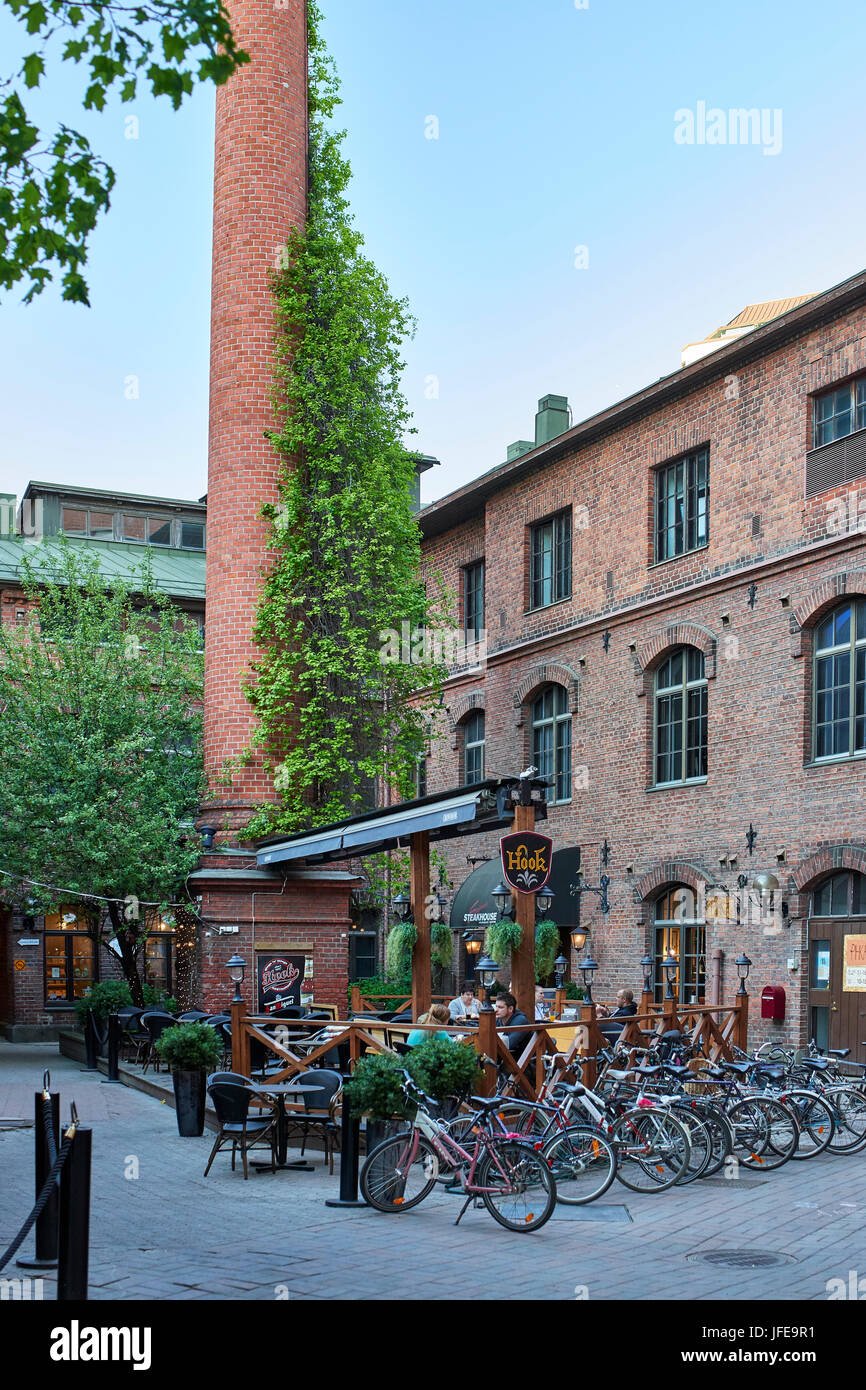 Courtyard caffetteria all'aperto e sala da pranzo su una tarda serata estiva a Tampere, impostare nel rinnovato vecchio rosso mattone edifici di fabbrica Foto Stock