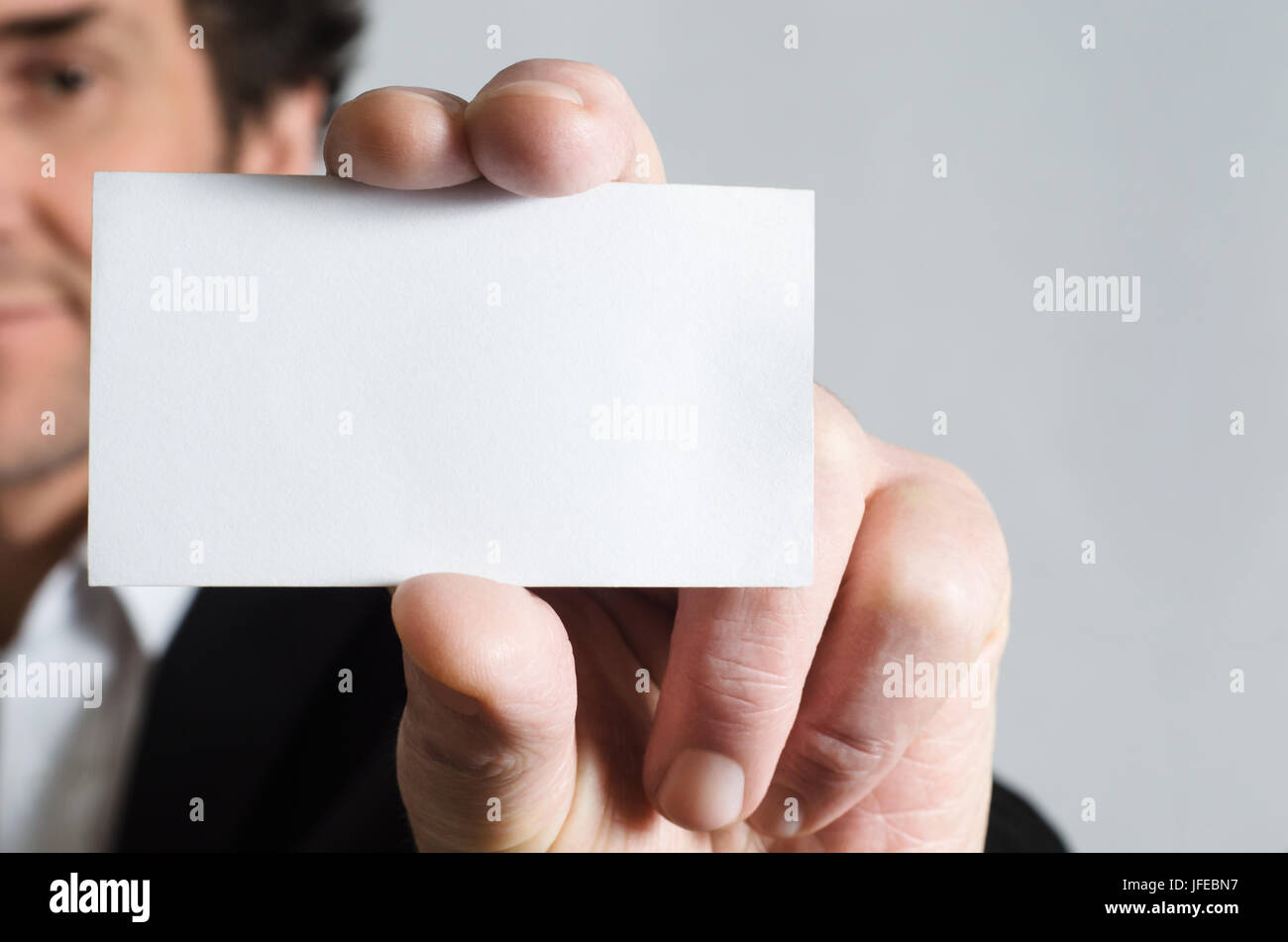 Un uomo in un abito nero con camicia bianca con in mano una blank business card per visualizzare nel visualizzatore. Foto Stock