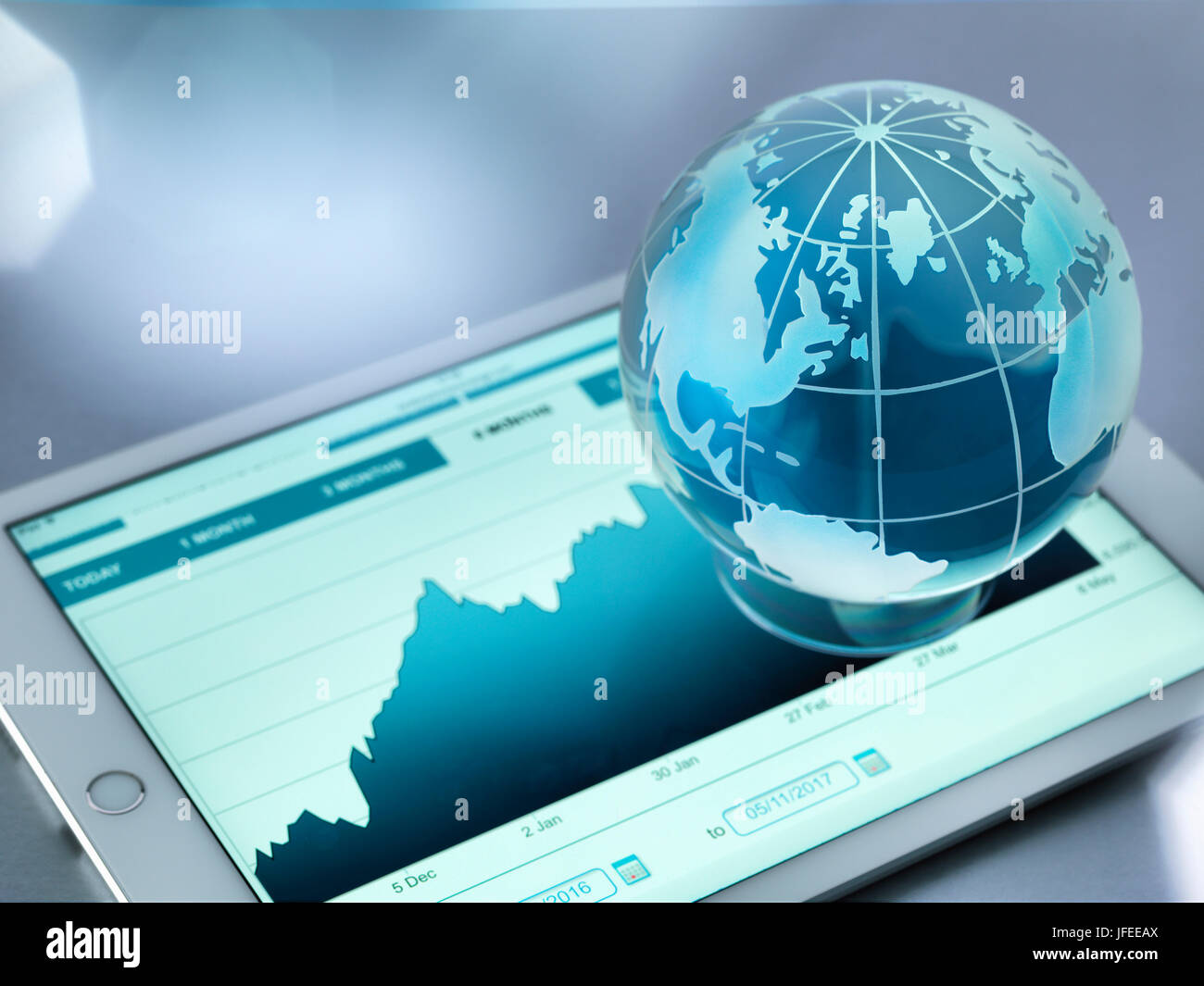 Un globo di vetro che illustra il mondo seduti su un tavolo digitale che mostra un aumento di prezzo di stock. Foto Stock