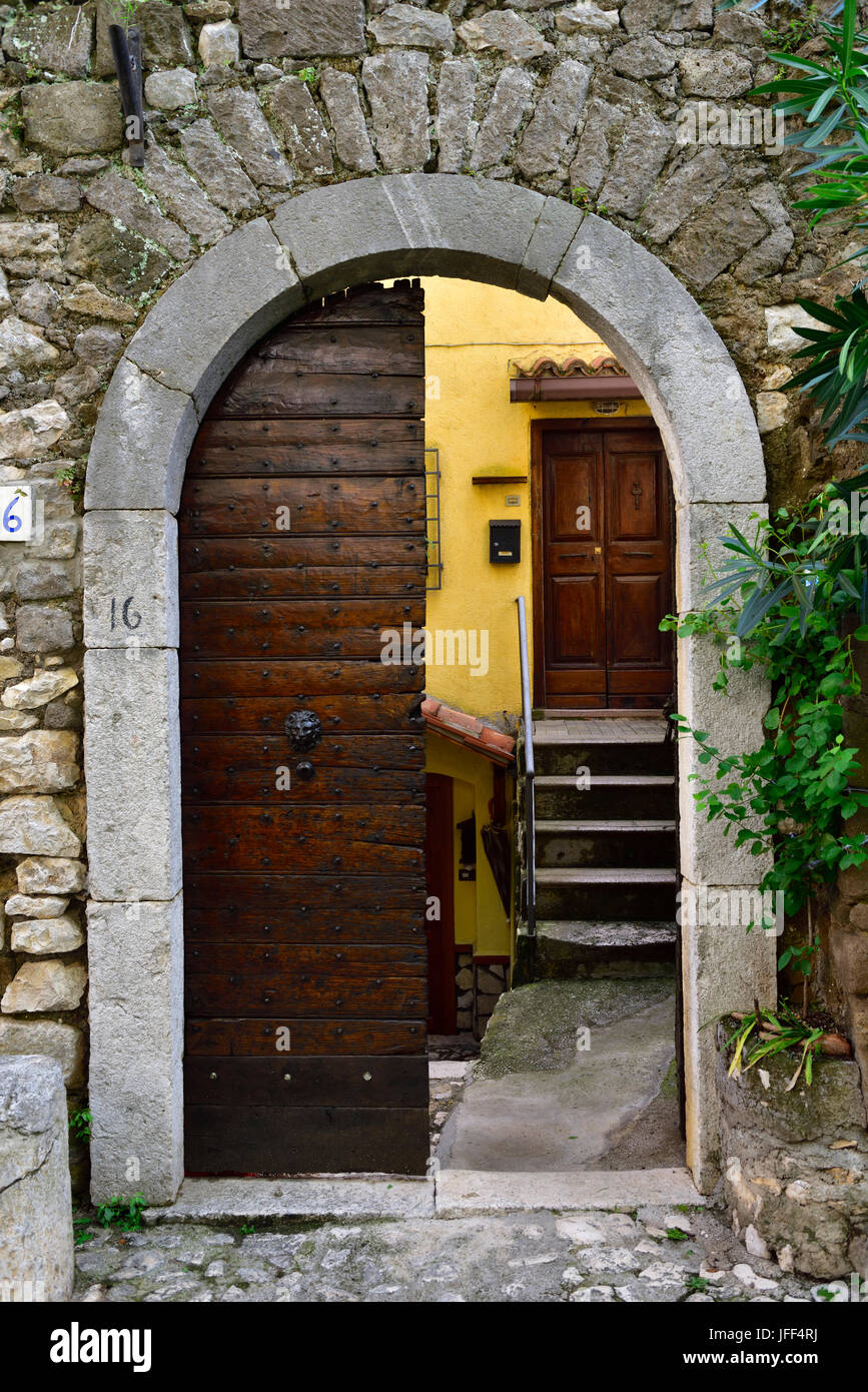 Visualizzazione attraverso l'arcata in pietra con porta in legno che conduce a gradini in pietra e un'altra porta di legno, la città medievale di Cori, Italia Foto Stock