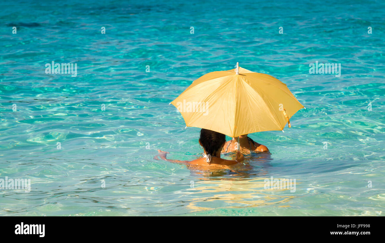 Due giovani donne asiatiche sotto un ombrello in piedi nel mare turchese Foto Stock
