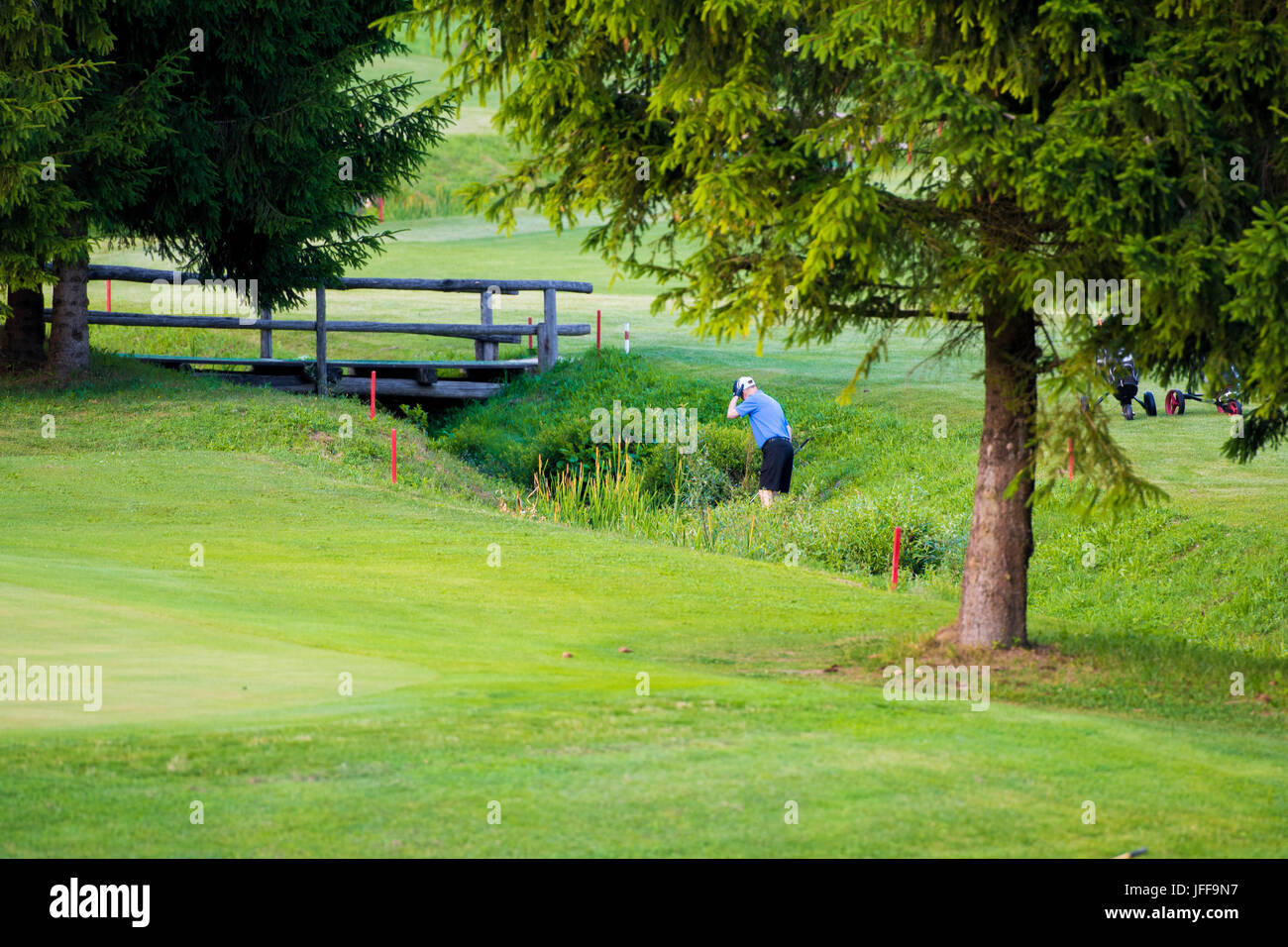 Giocatore di Golf, rivolta lontano dal visualizzatore, ricerca di palla persa nel flusso di acqua e di erba alta Foto Stock