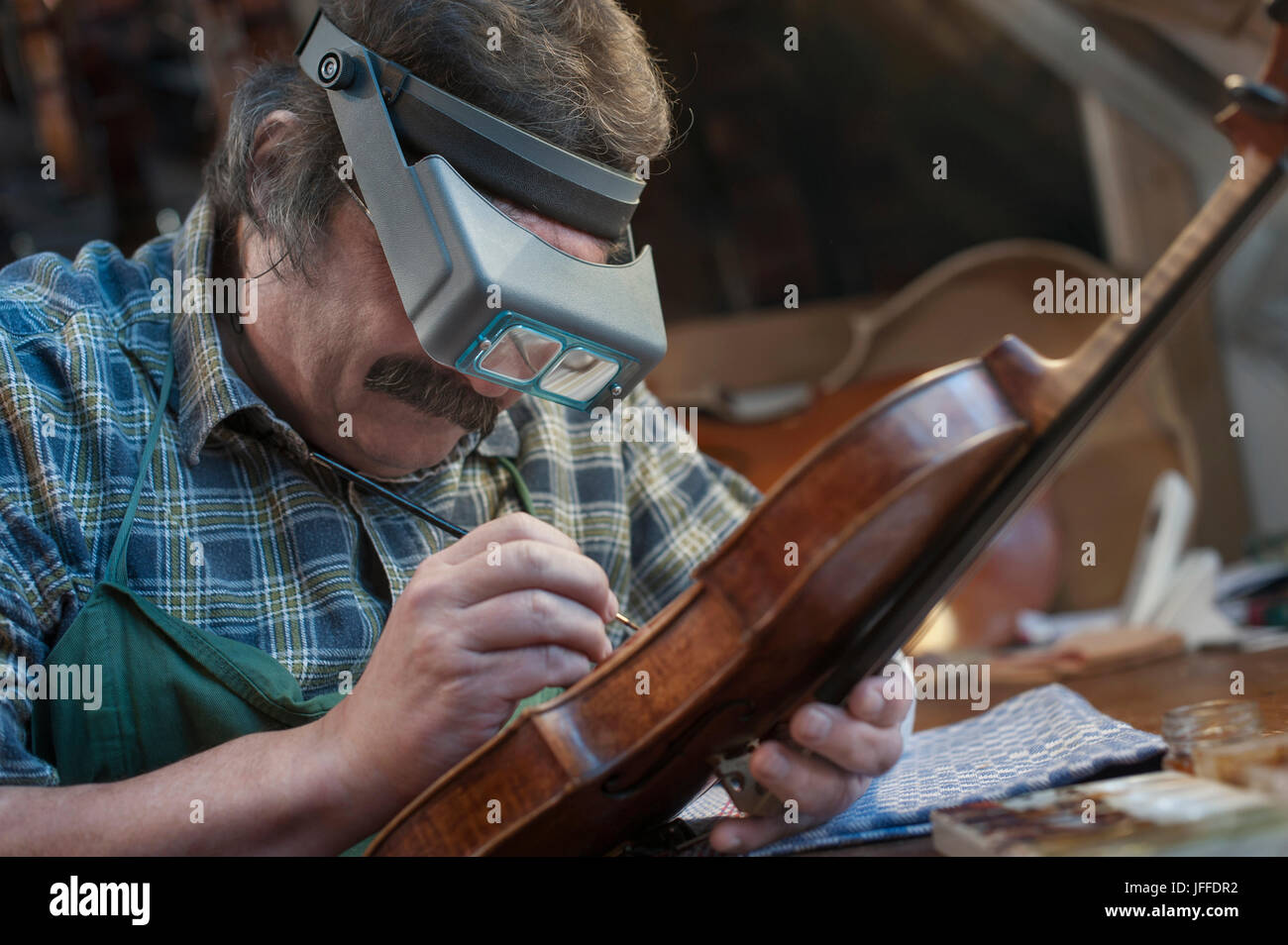 Liutaio pittura violino utilizzando una lente di ingrandimento Foto Stock