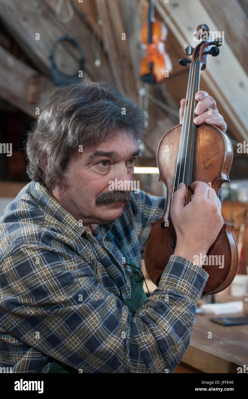 Artigiano esaminando violino in officina Foto Stock