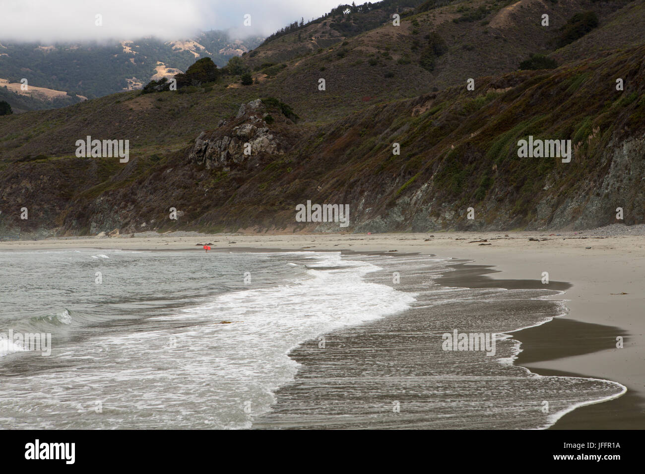 Onde e surf vieni a terra sul Big Sur Costa. Un nuotatore solitario, boarder, sorge nell'acqua. Foto Stock