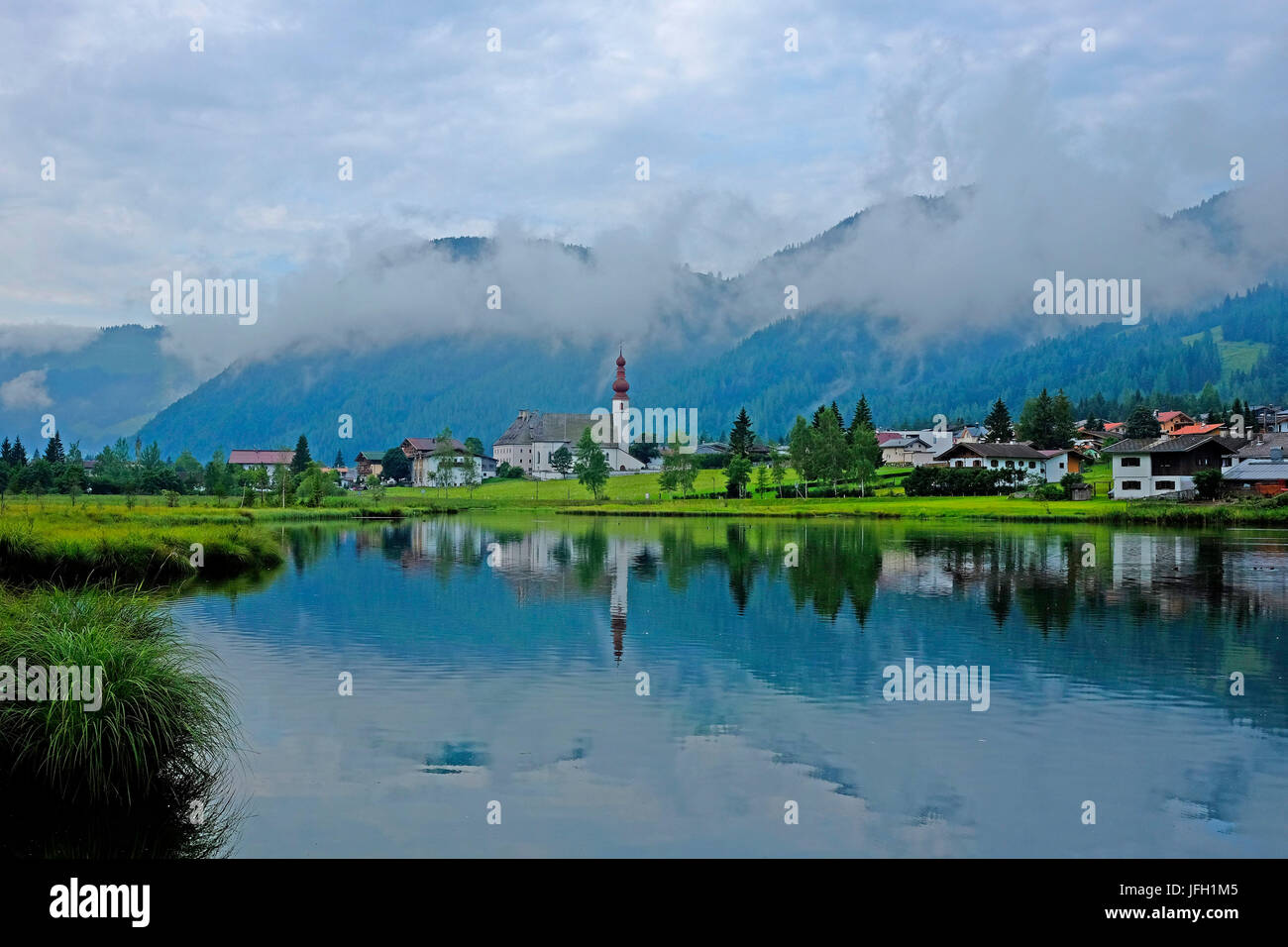 Atmosfera mattutina in montagna lago Pillersee con st Ulrich, chiesa si rispecchia nel lago, ascendente nebbia mattutina, montagne boschive, Pillerseetal, Tirolo, Austria Foto Stock