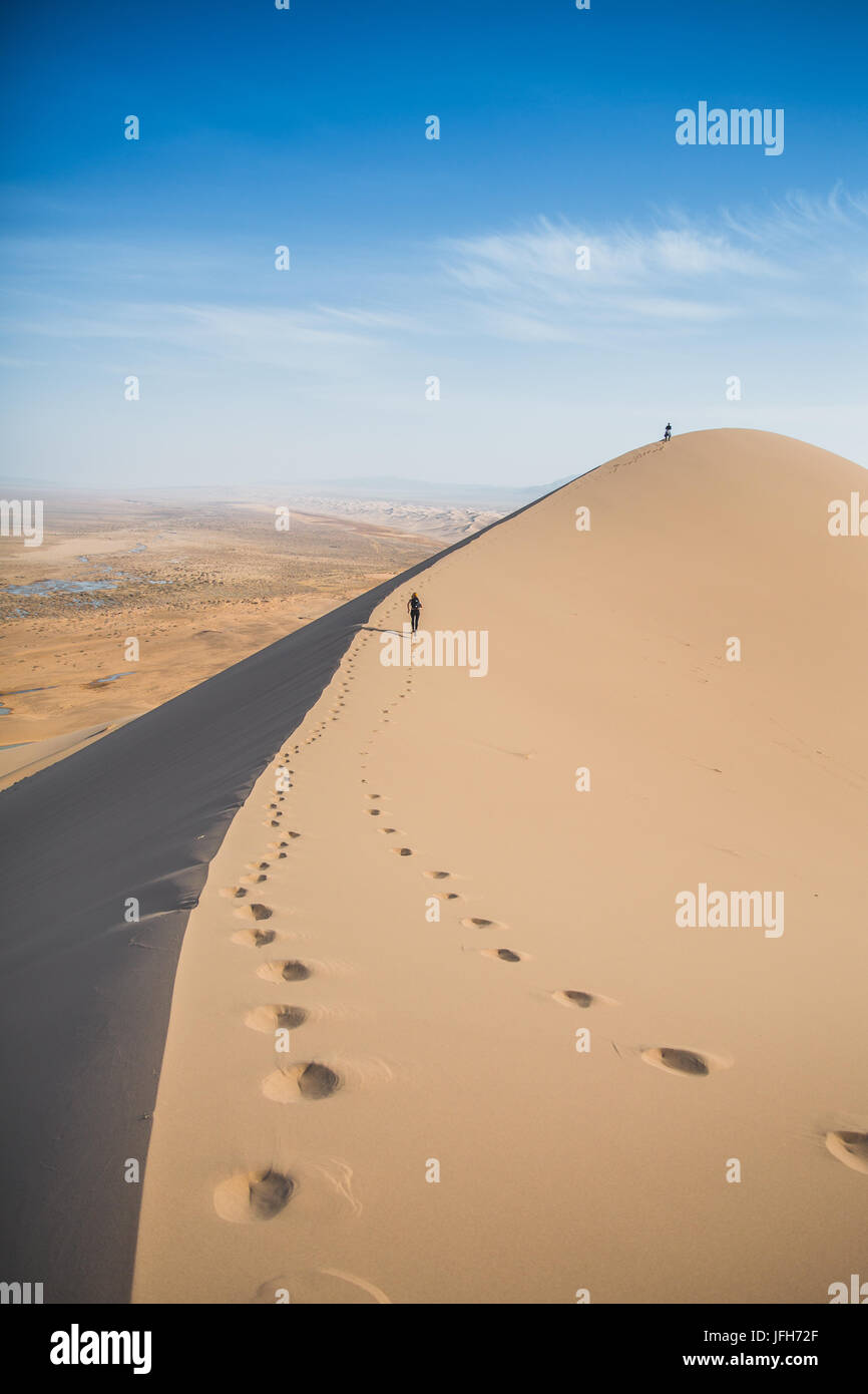 Due amici in esecuzione dopo ogni altro su di una duna di sabbia nel deserto del Gobi, Mongolia Foto Stock