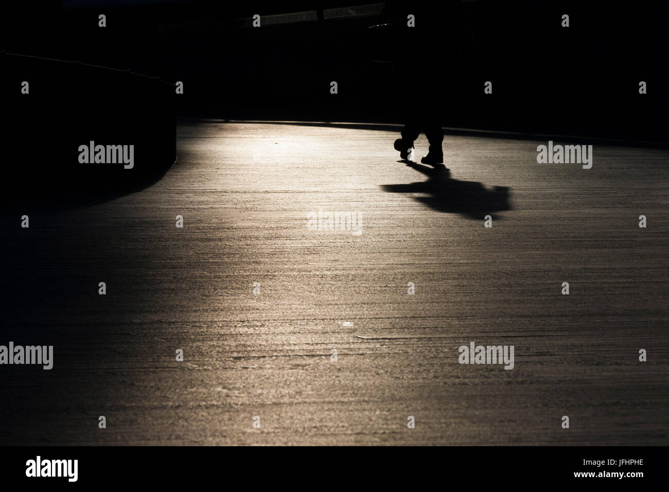 Un uomo cammina attraverso un'area pavimentata in silhouette con il sole che tramonta dietro di lui Foto Stock