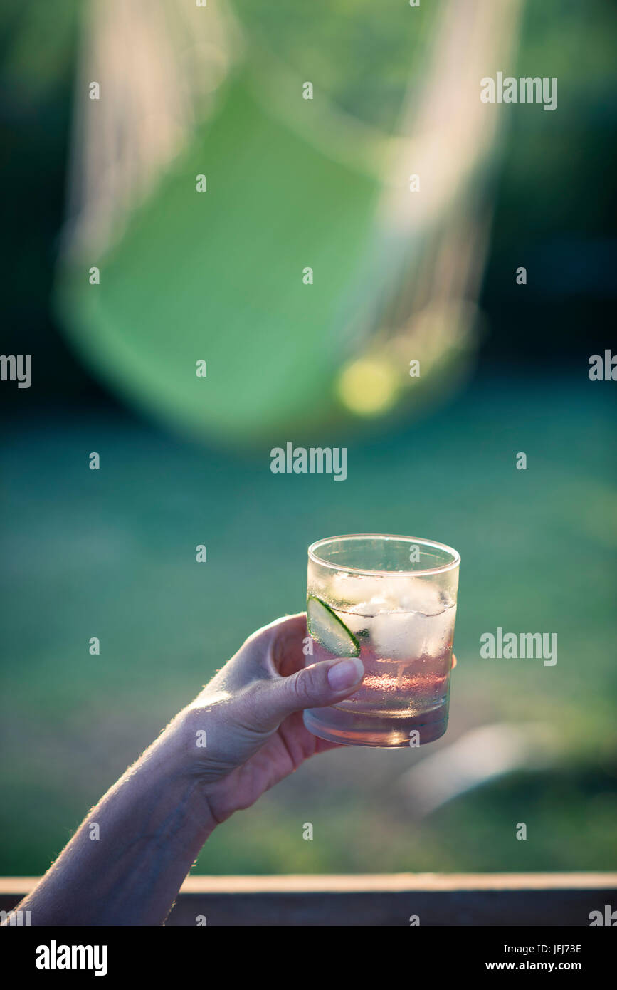 Il gin tonic in mano nella luce della sera Foto Stock