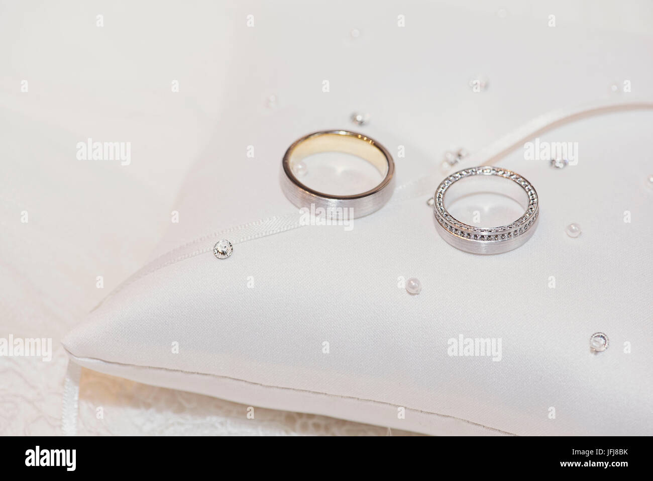 Gli anelli di nozze in oro e platino con diamanti su un piccolo cuscino con perle Foto Stock
