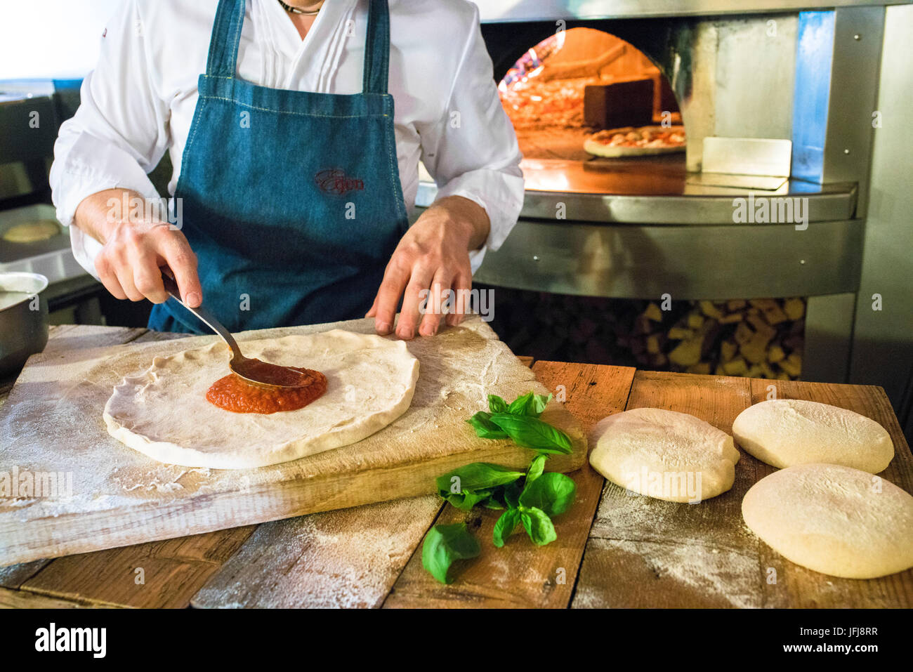 Lo chef riempie la pizza con salsa di pomodoro e gli ingredienti freschi  quindi pronto per essere cotto al forno a legna Italia Foto stock - Alamy