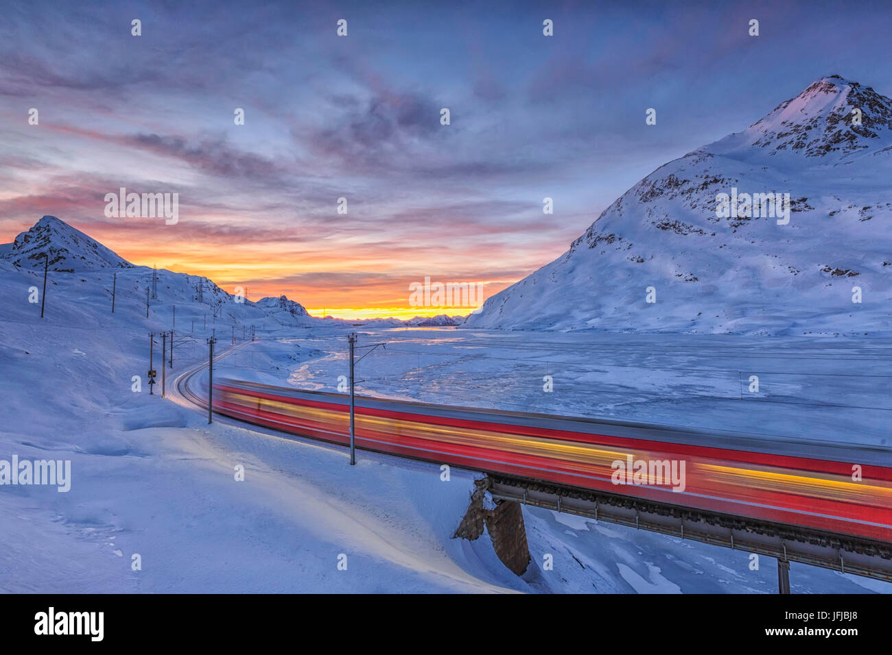 Il Bernina Express passa sulle rive del Lago Bianco completamente congelato prima che il sole sorge nel Cantone dei Grigioni, Engadina, Svizzera, Europa Foto Stock