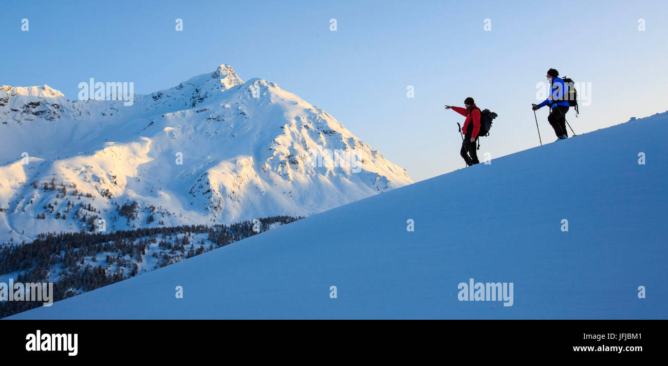 Escursionista con le racchette da neve guarda il Piz de la Margna accesa dall'ultimo sole del giorno del Cantone dei Grigioni, Maloja Pass, Engadina, Svizzera, Europa Foto Stock