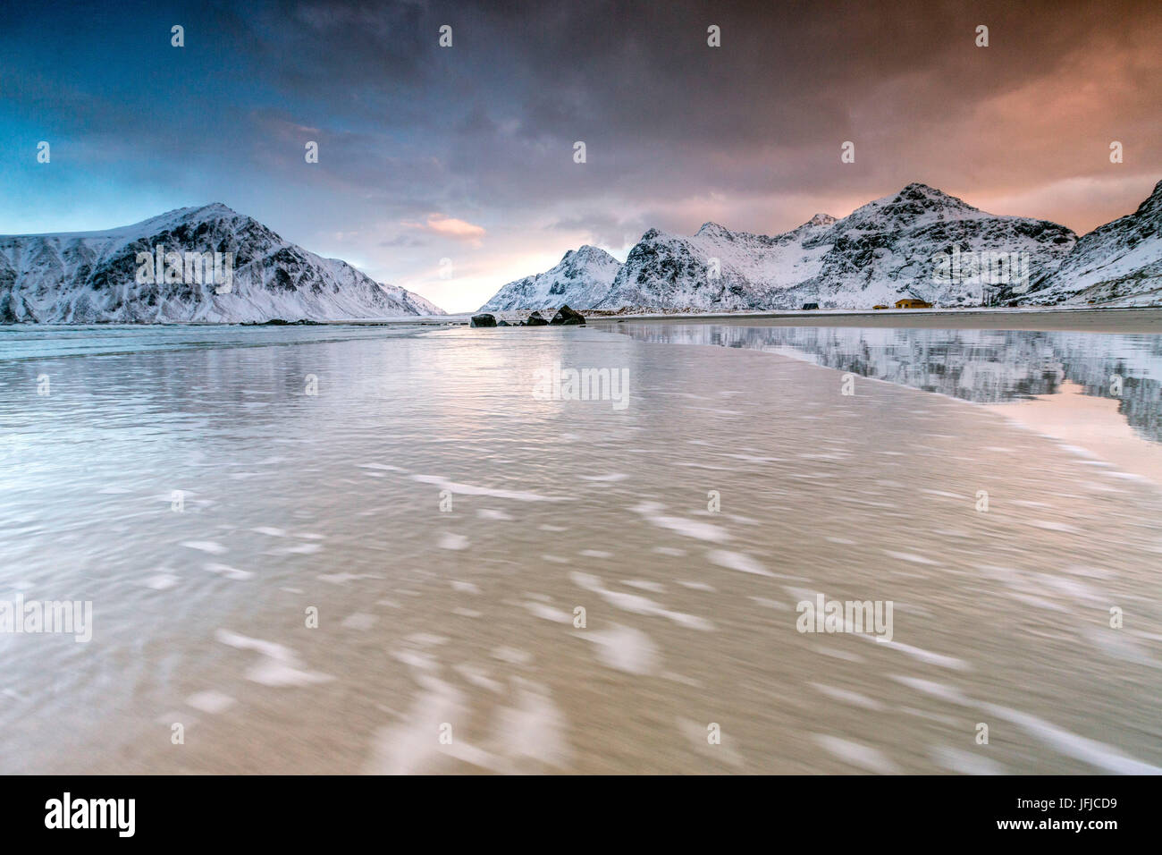 Cielo rosa nel surreale Skagsanden spiaggia circondata da montagne coperte di neve, Isole Lofoten Norvegia del Nord Europa Foto Stock