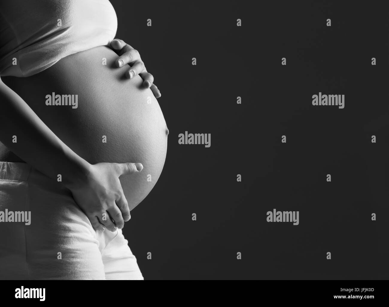 Ventre della donna incinta monocromatico su uno sfondo scuro Foto Stock