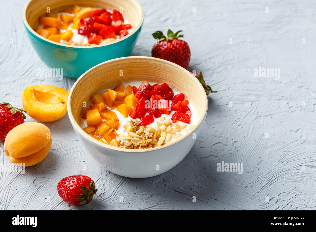 Lo yogurt naturale con pezzi di Albicocche Fragole, granola e pinoli in due ciotole su sfondo chiaro Foto Stock