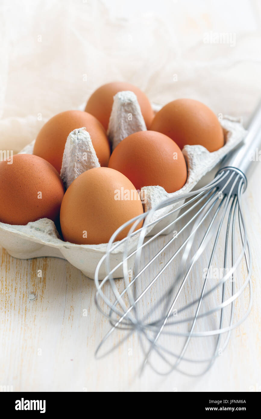 Scatola con le uova e mescolare con una frusta bianco su un tavolo di legno. Foto Stock