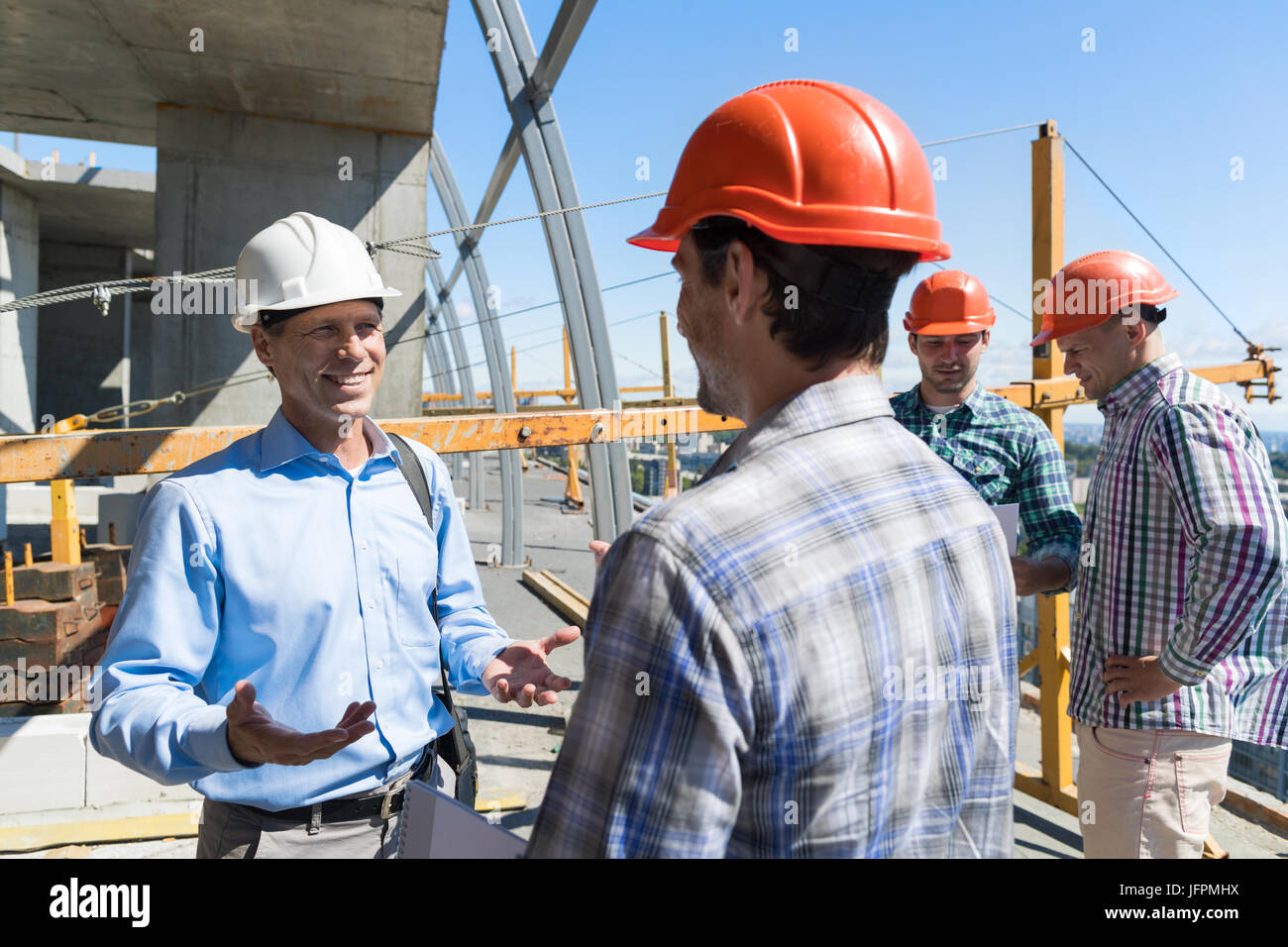 Costruttori incontro sul sito di costruzione architetto parlando con l'Appaltatore oltre il gruppo di apprendista Foto Stock