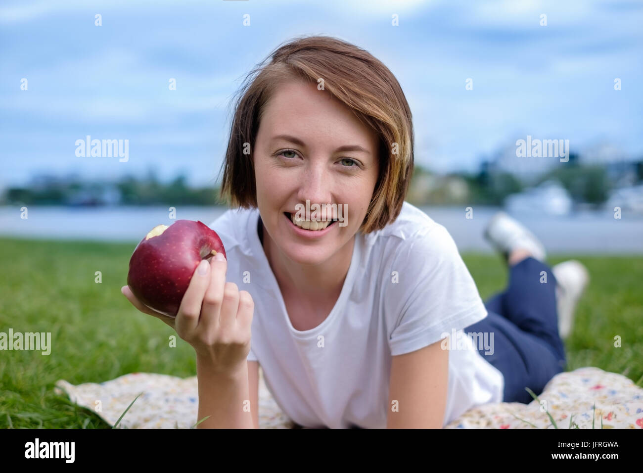Molto bello il modello caucasico mangiare red apple nel parco. All'esterno ritratto della bella ragazza giovane Foto Stock