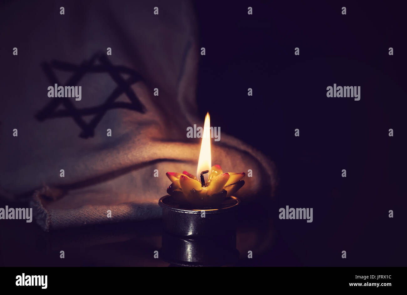 La stella di Davide e la candela si erge sulla tavola su uno sfondo nero in memoria delle vittime dell'Olocausto e il genocidio. Foto Stock