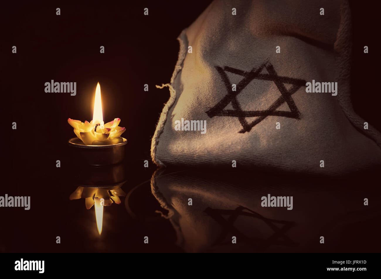 Una candela che brucia accanto alla stella di Davide su uno sfondo nero. Un simbolo in ricordo delle vittime del genocidio degli ebrei nel terzo Reich Foto Stock