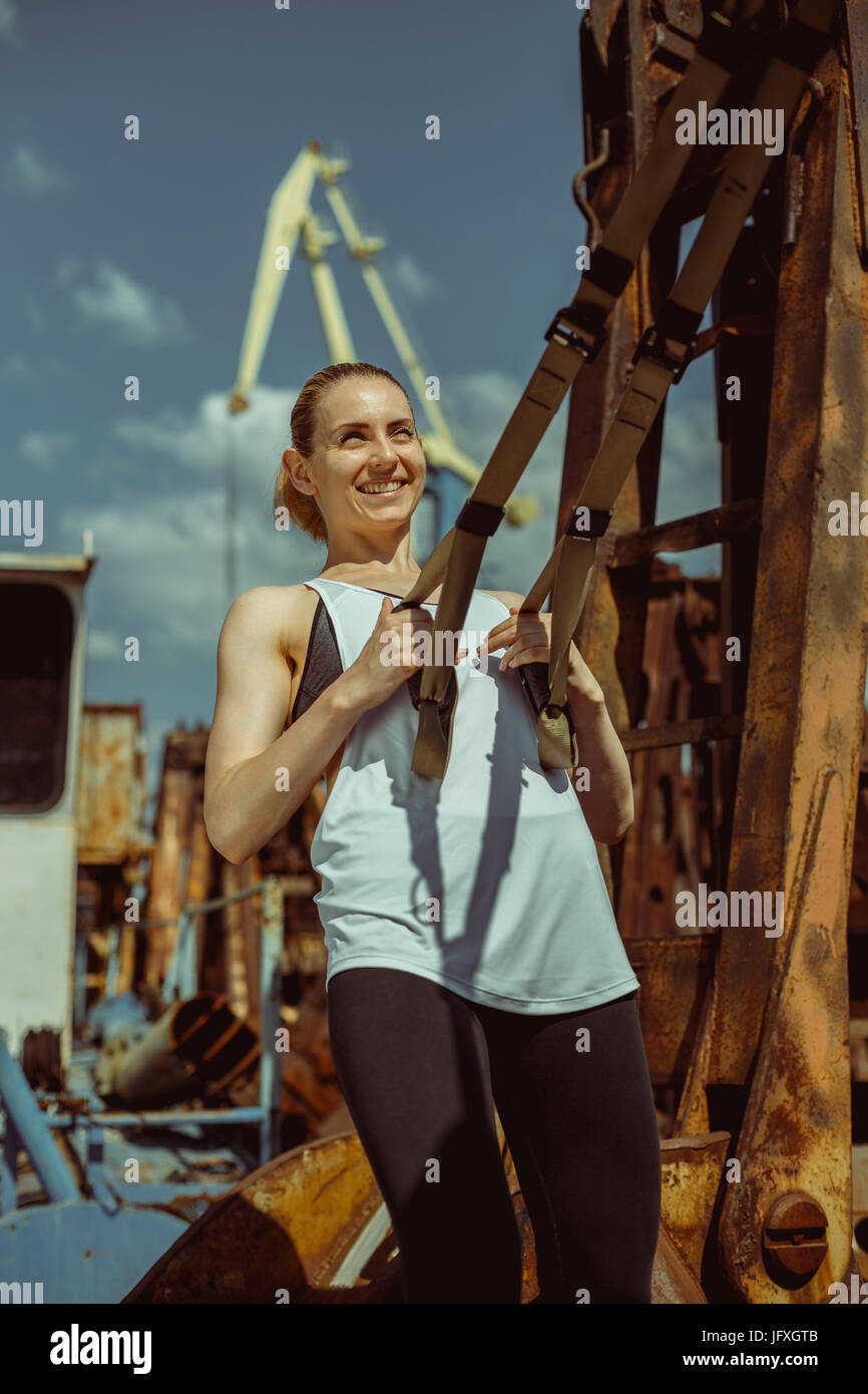 Athletic donna fare trx esercitare contro lo sfondo di un porto marittimo Foto Stock