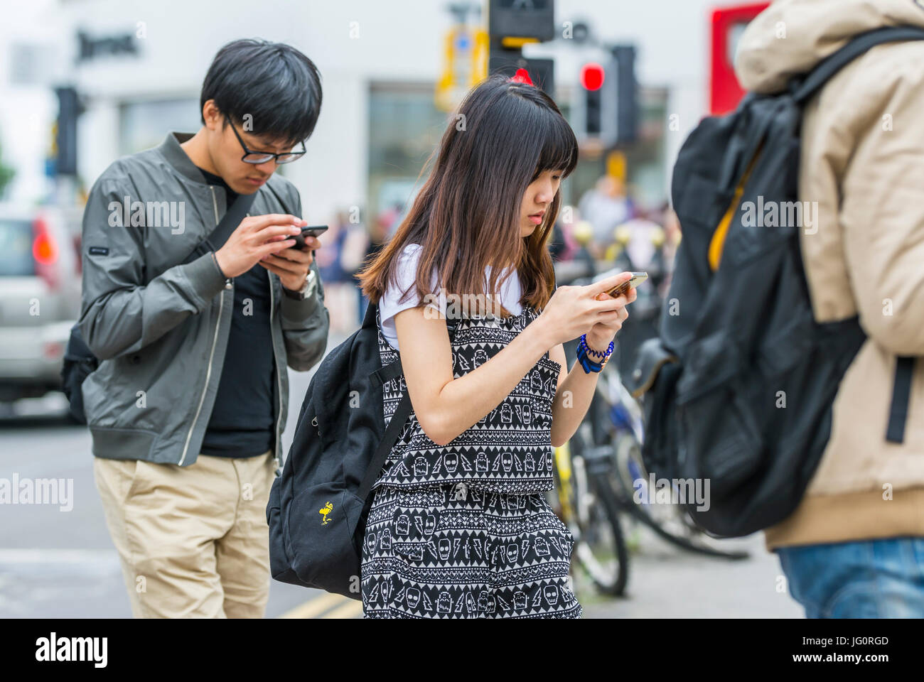 Sempre connesso concetto. I turisti giapponesi a camminare in una città mentre guardando verso il basso e usando il loro smartphone. Foto Stock