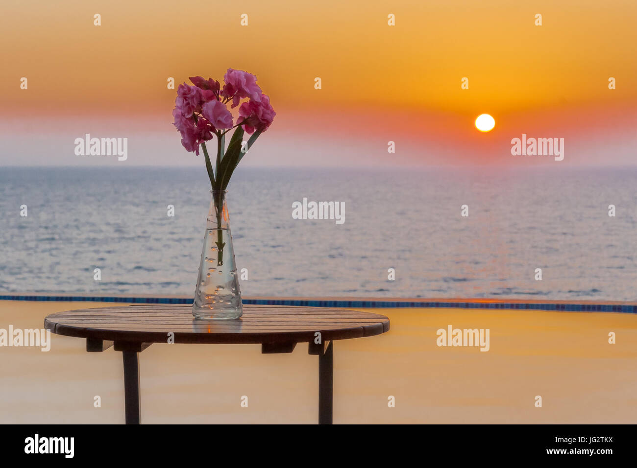 Vaso di fiori sul tavolo a bordo piscina con vista sul mare al tramonto nel villaggio di Pomos, area di Paphos, Cipro Foto Stock