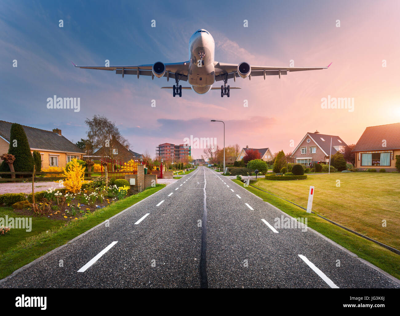 Bellissimo paesaggio con passeggero aereo è volare nel cielo di tramonto sopra la strada asfaltata attraverso la città con le case e i cortili al tramonto Foto Stock