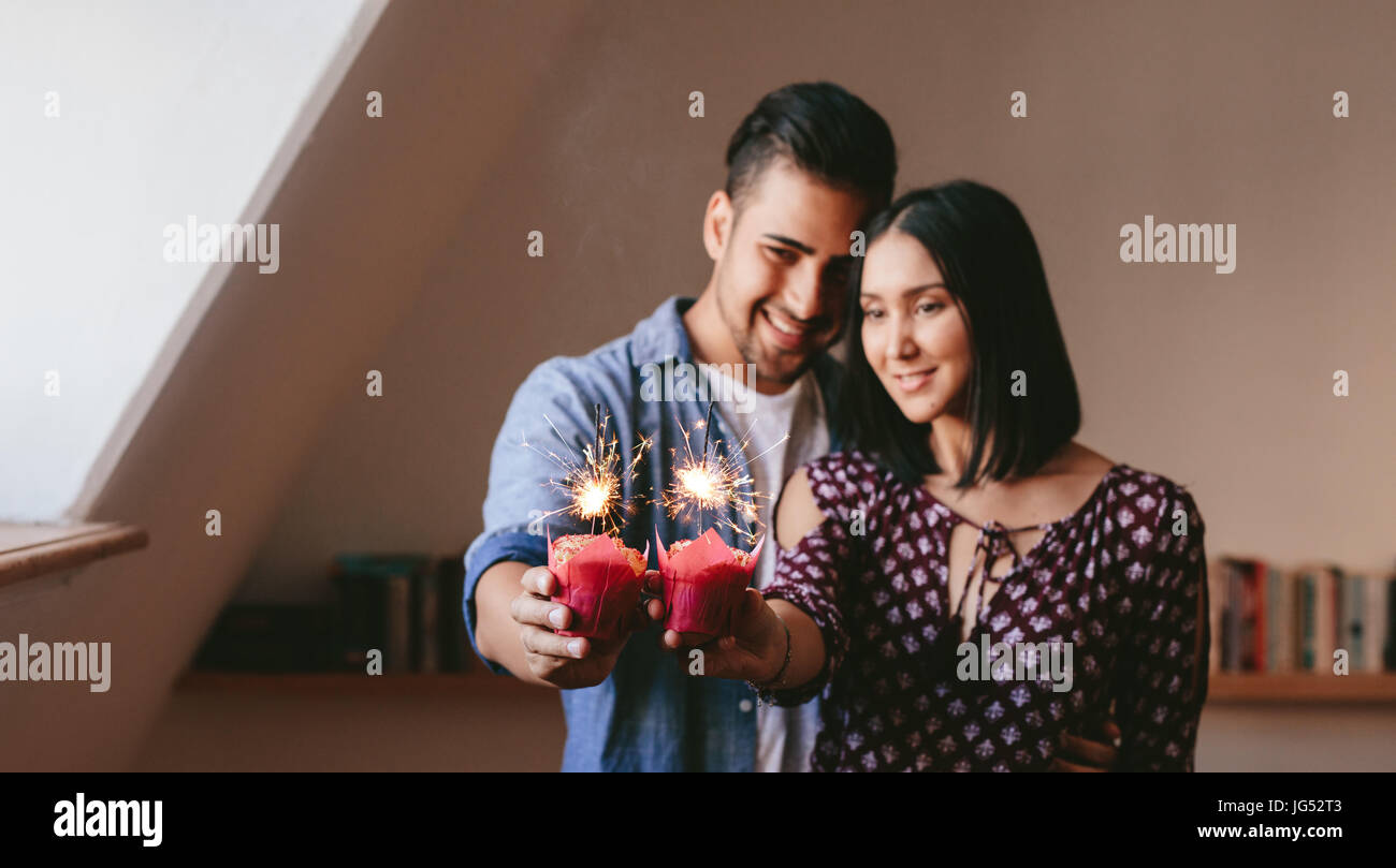 Coppia giovane azienda due tortine e che festeggiano il loro anniversario. Tortine con botti nelle mani del giovane in piedi insieme a casa. Foto Stock