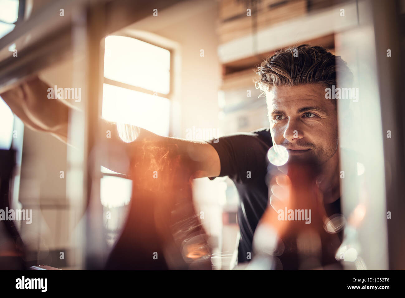 Colpo di giovane uomo che lavora sulla birra macchina imbottigliatrice alla birreria fabbrica. Birraio maschio di controllo del processo di fabbricazione della birra in fabbrica. Foto Stock