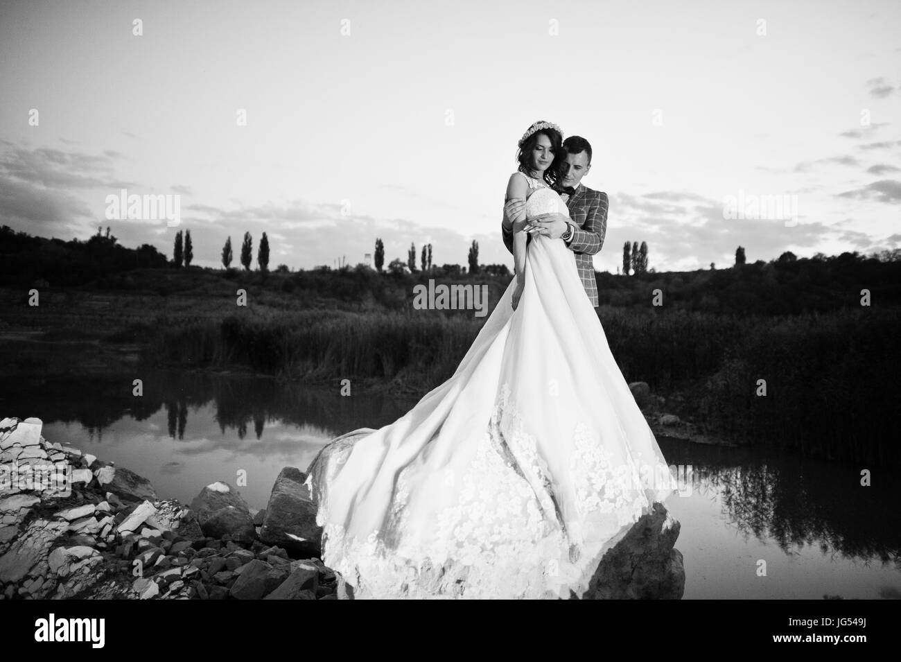 Bella sposi tenendo le mani e guardando ogni altro nella campagna accanto al lago di sera. Foto in bianco e nero. Foto Stock