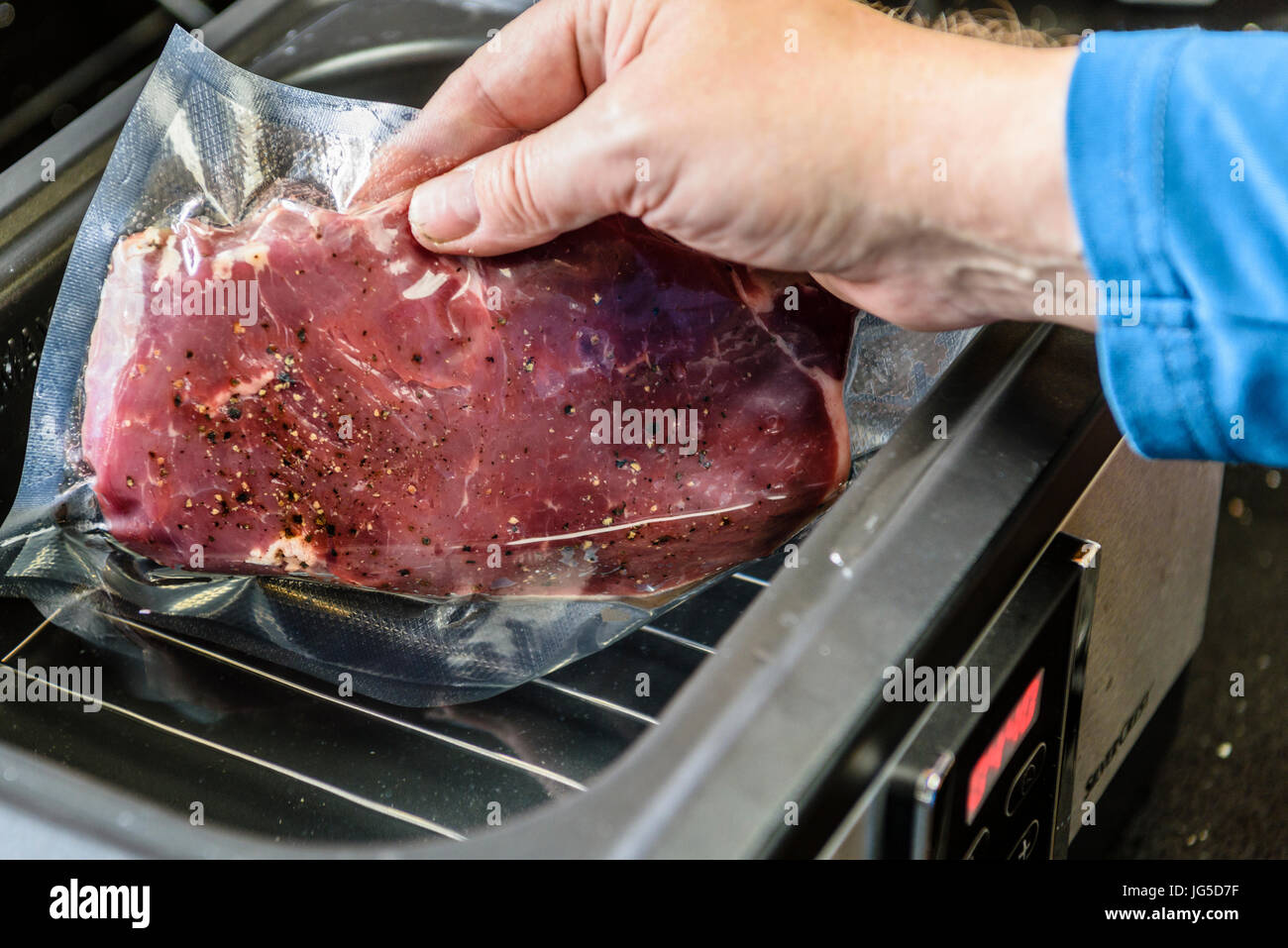 Una persona che mette una bistecca di controfiletto all'interno di un vuoto sacchetto sigillato in un sous vide bagno d'acqua per cucinare a 55C. Foto Stock