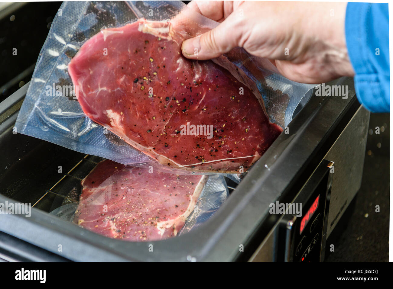 Una persona che mette una bistecca di controfiletto all'interno di un vuoto sacchetto sigillato in un sous vide bagno d'acqua per cucinare a 55C. Foto Stock