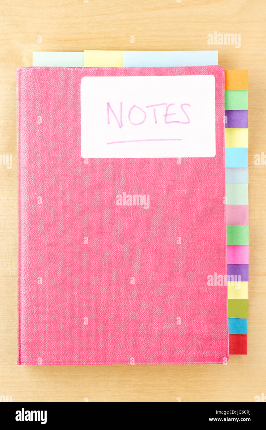 Notebook rosa su un legno chiaro dello sfondo. White " Note " etichetta sul coperchio, tre divisori a linguetta di sezionamento libro lungo il bordo superiore e quindici lungo diritto sid Foto Stock