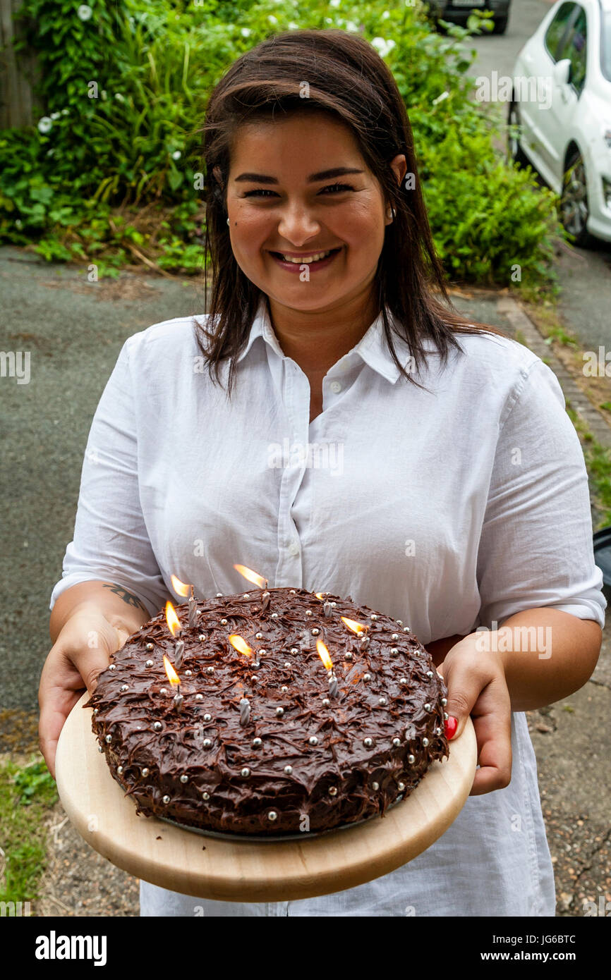 Una giovane donna in piedi su una porta in possesso di una torta di compleanno, Sussex, Regno Unito Foto Stock