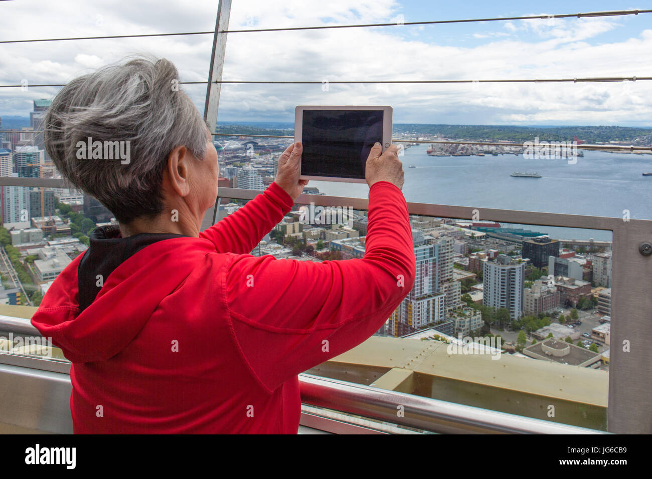 Donna con i capelli grigi è di scattare una foto con il suo tablet iPad della vista dalla Space Needle a Seattle, Washington Foto Stock