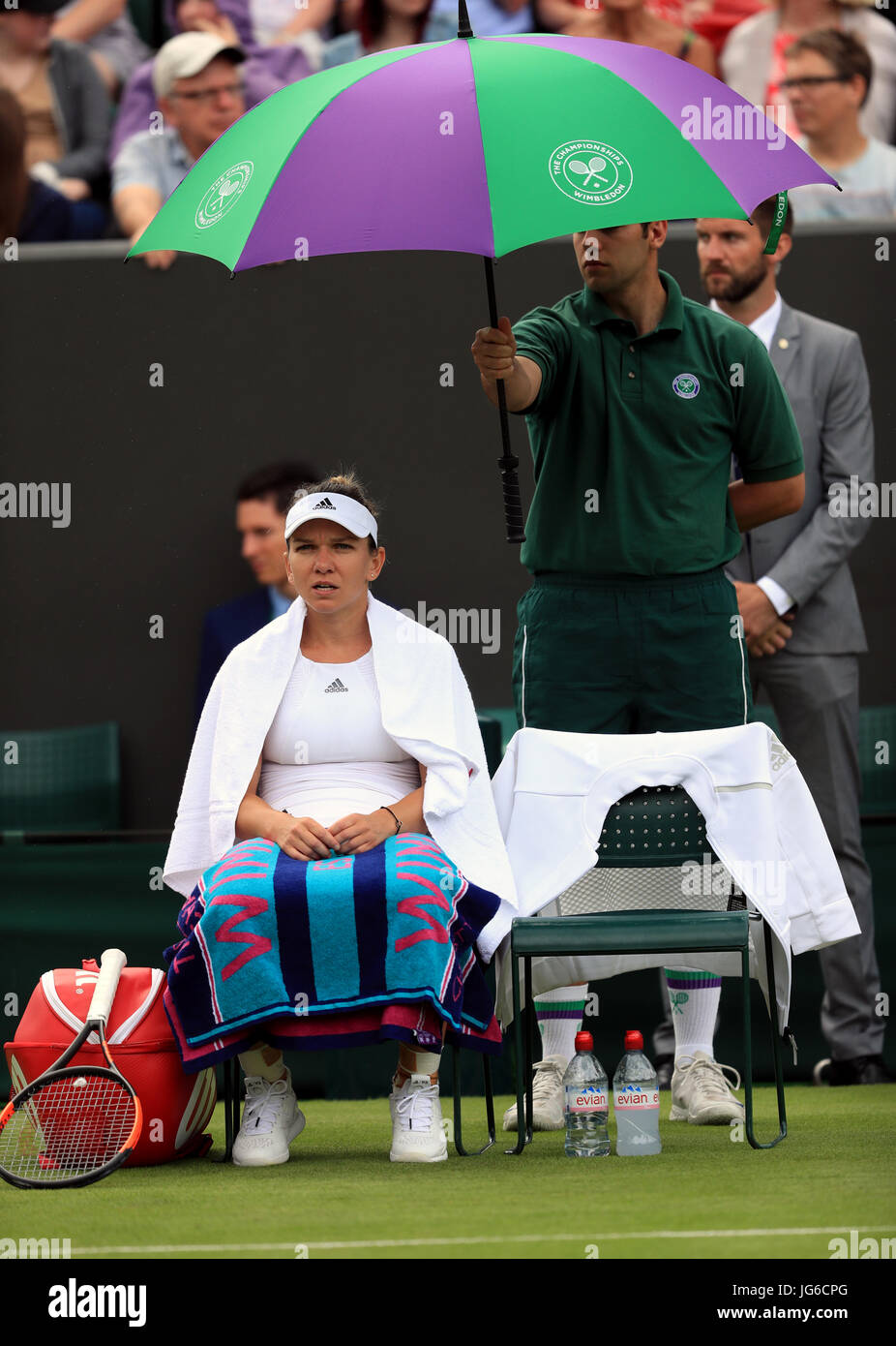 Simona Halep è coperto da un ombrello come pioggia inizia a cadere durante la sua partita contro Marina ERAKOVIC il giorno uno dei campionati di Wimbledon al All England Lawn Tennis e Croquet Club, Wimbledon. Foto Stock