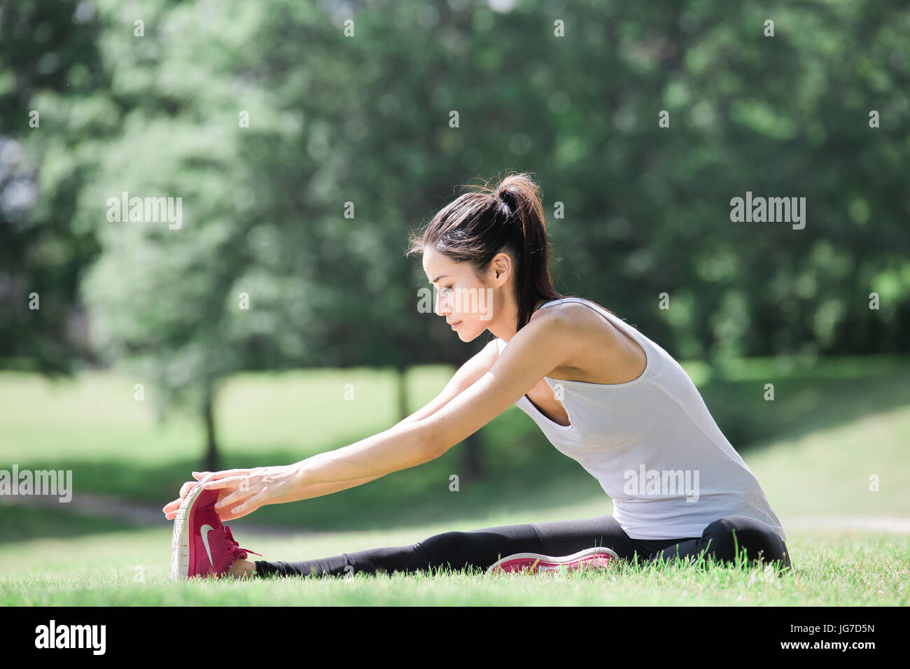 Una giovane e bella donna asiatica stretching, esercizio e fare yoga outdoor in un parco Foto Stock