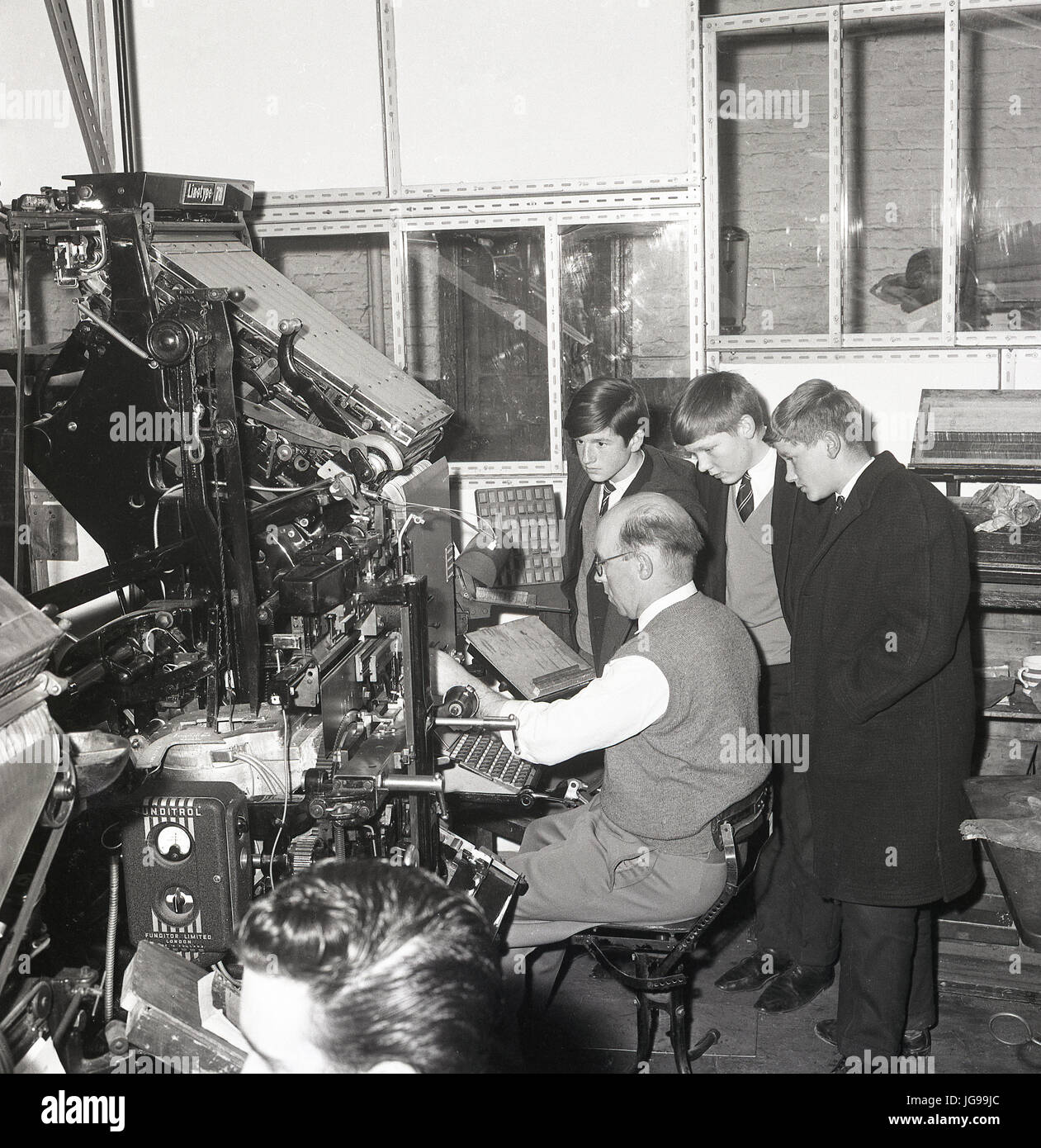 Anni 60, tre ragazzi della scuola guardano un giornale tipografo o compositor al lavoro durante una visita alle presse di stampa del South East London e del giornale Kentish Mercury, Inghilterra, Regno Unito. Foto Stock