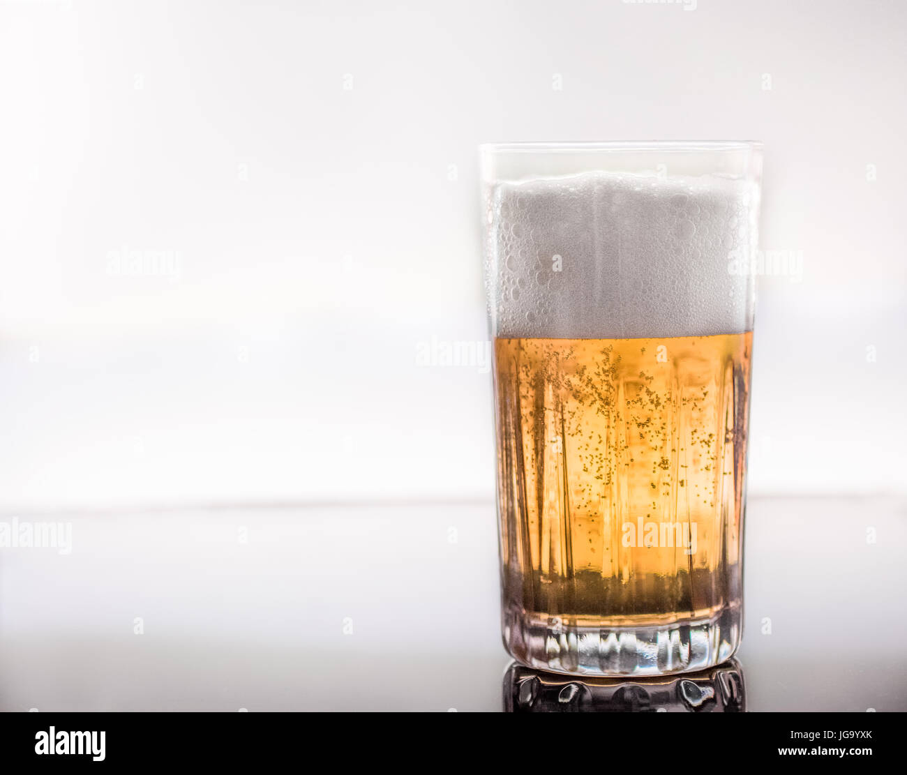 Freddo e una deliziosa birra versata in un vetro trasparente su un vetro riflettente superficie, retroilluminato Foto Stock
