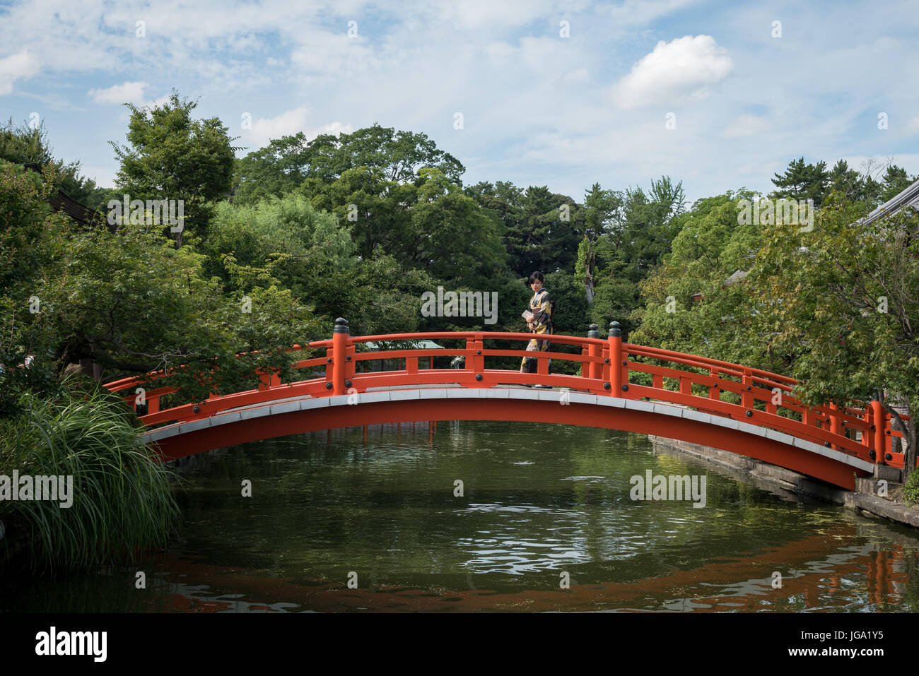 Donna in kimono attraversando ponte rosso. Giardino e acqua, Tokyo, Giappone Foto Stock