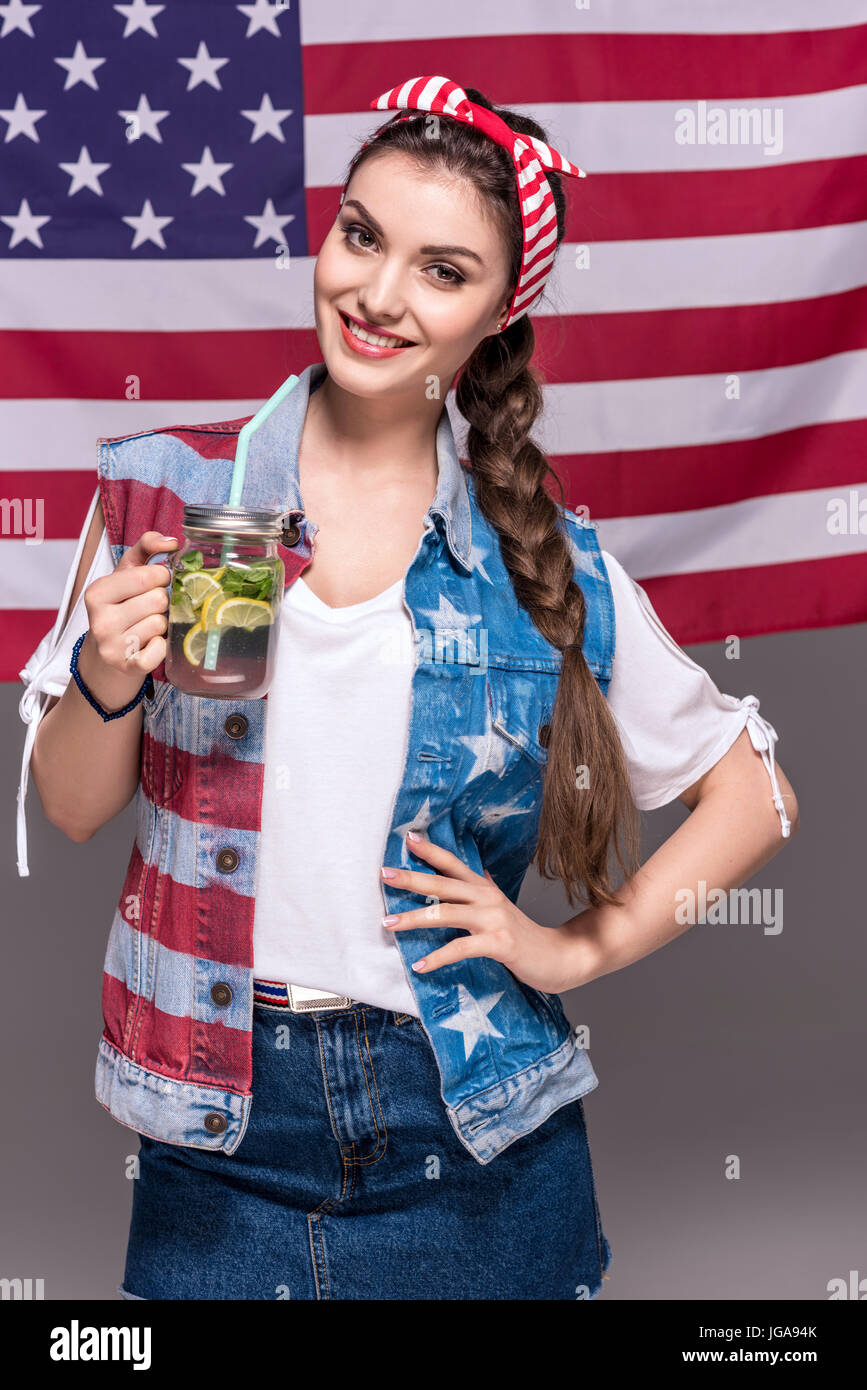 Ritratto di donna sorridente holding drink in mano con bandiera americana dietro Foto Stock